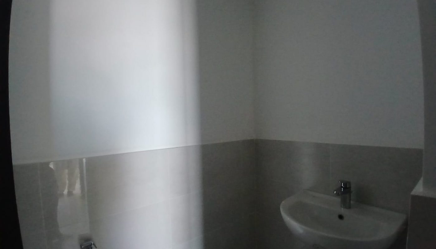 A small bathroom with white tiled walls, a wall-mounted sink with a faucet, and a handheld bidet spray attached beside it.
