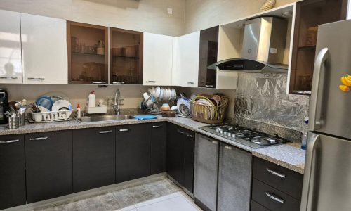 A modern kitchen with dark wood cabinets, white upper cabinets, stainless steel appliances, a double-basin sink, and various kitchen items organized on the countertop.