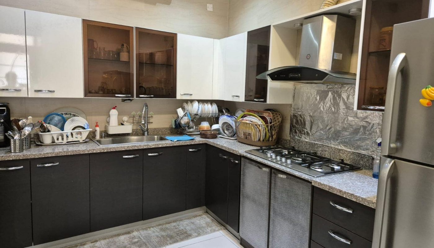 A modern kitchen with dark wood cabinets, white upper cabinets, stainless steel appliances, a double-basin sink, and various kitchen items organized on the countertop.