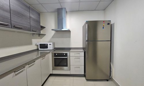 A modern kitchen with gray cabinetry, a stainless steel refrigerator, an oven, a stove, a microwave, and an exhaust hood. The space has a tiled floor and a white ceiling.