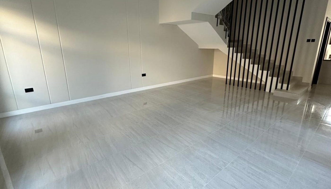 Empty modern room with light gray tile flooring, a minimalist staircase, and a small chandelier. Walls are plain and there are no furnishings.
