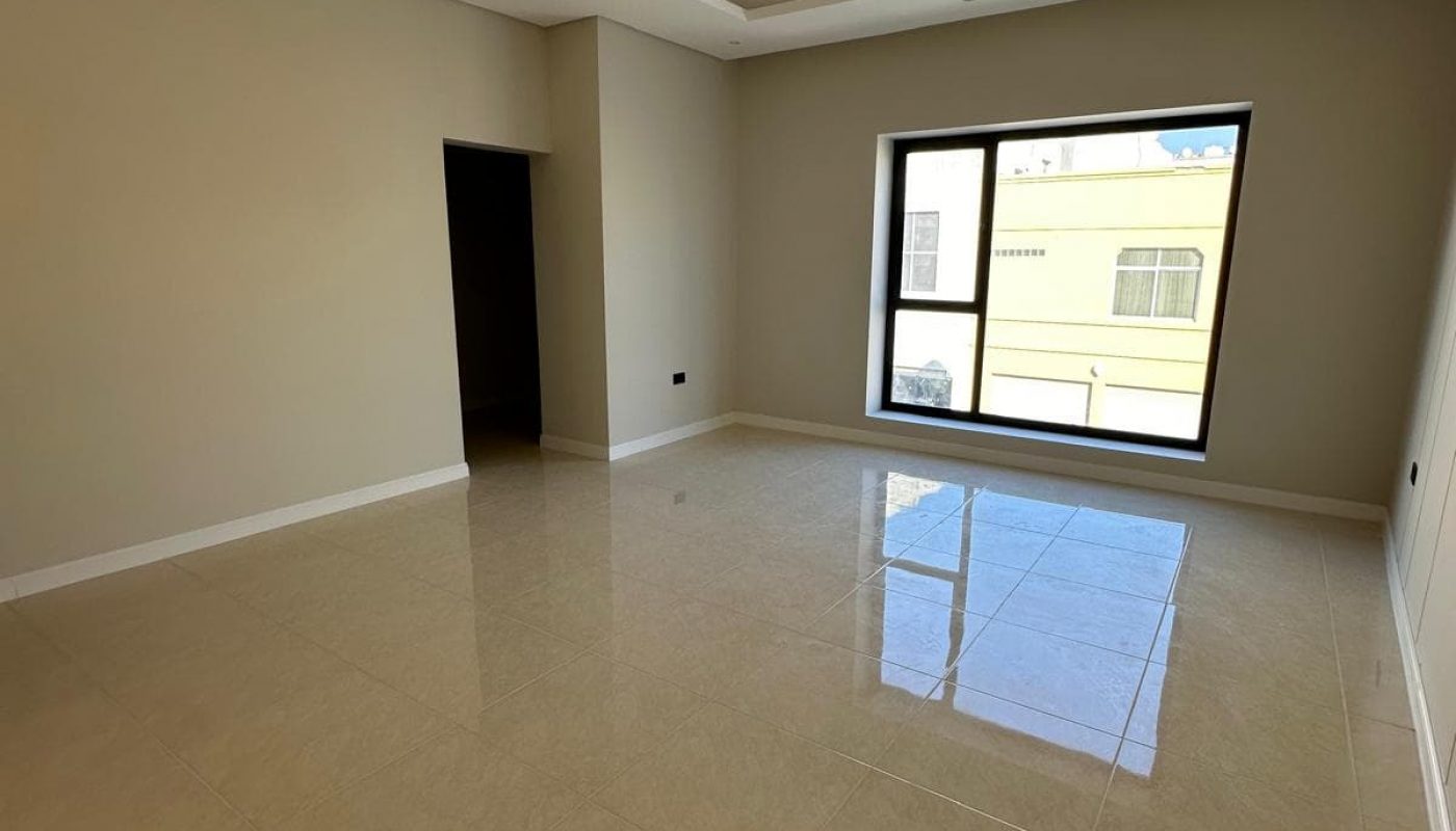 An empty room with beige tiled floor, beige walls, a large window, and a recessed ceiling light fixture.