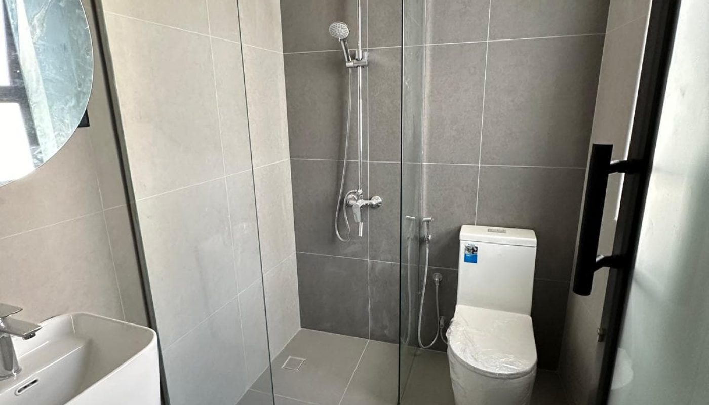 Modern bathroom with gray tiles, featuring a shower with a glass partition, a wall-mounted sink, and a toilet.