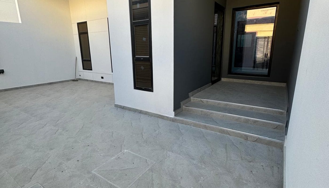 Spacious modern building exterior with a stone-tiled courtyard, two entrances, one with steps, and large windows.