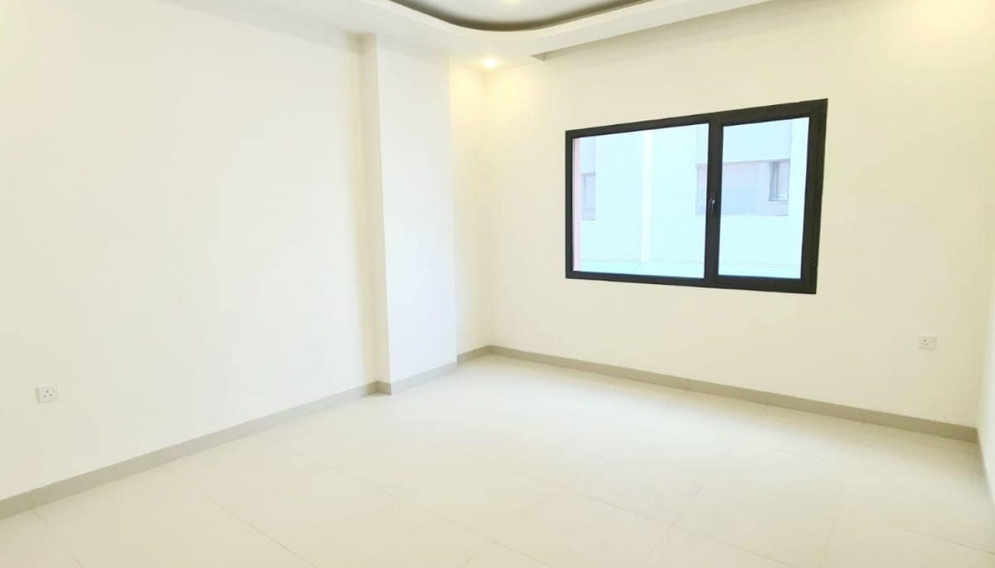 Empty room with light-colored tiled floor, white walls, recessed ceiling lights, and a window with a black frame on one wall.