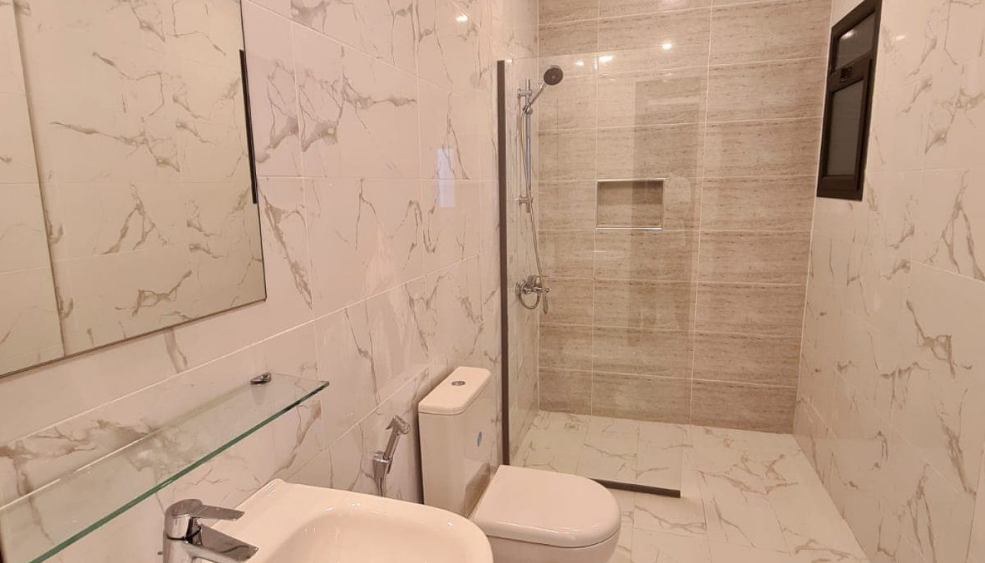 Modern bathroom with marble-patterned tiles, a wall mirror above a white sink, a toilet, and a glass-enclosed shower area.