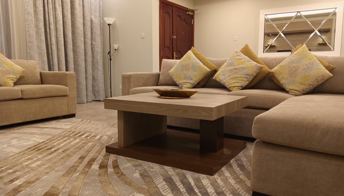 Modern living room with beige sofas, yellow patterned cushions, a wooden coffee table, decorative rug, floor lamp, and a wall mirror.