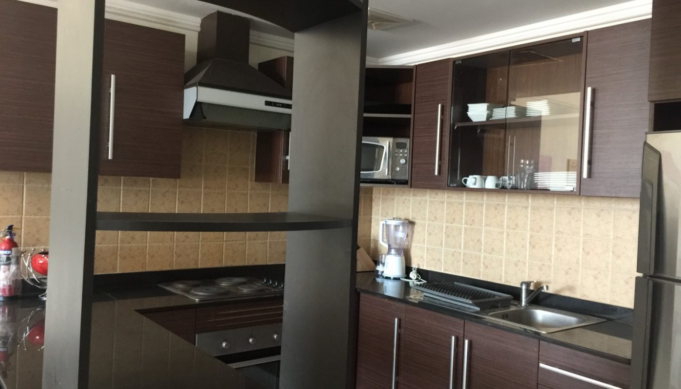 Modern kitchen with dark wood cabinets, stainless steel appliances, a blender on the counter, an electric stove, and beige tiled backsplash. Open shelves divide the space.