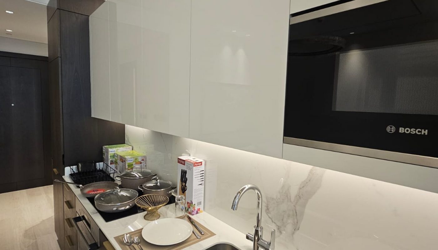 Modern kitchen with white cabinets, a sink, Bosch microwave, and stove. Table settings for two are placed on the counter, along with cereal, cookware, and a glass.