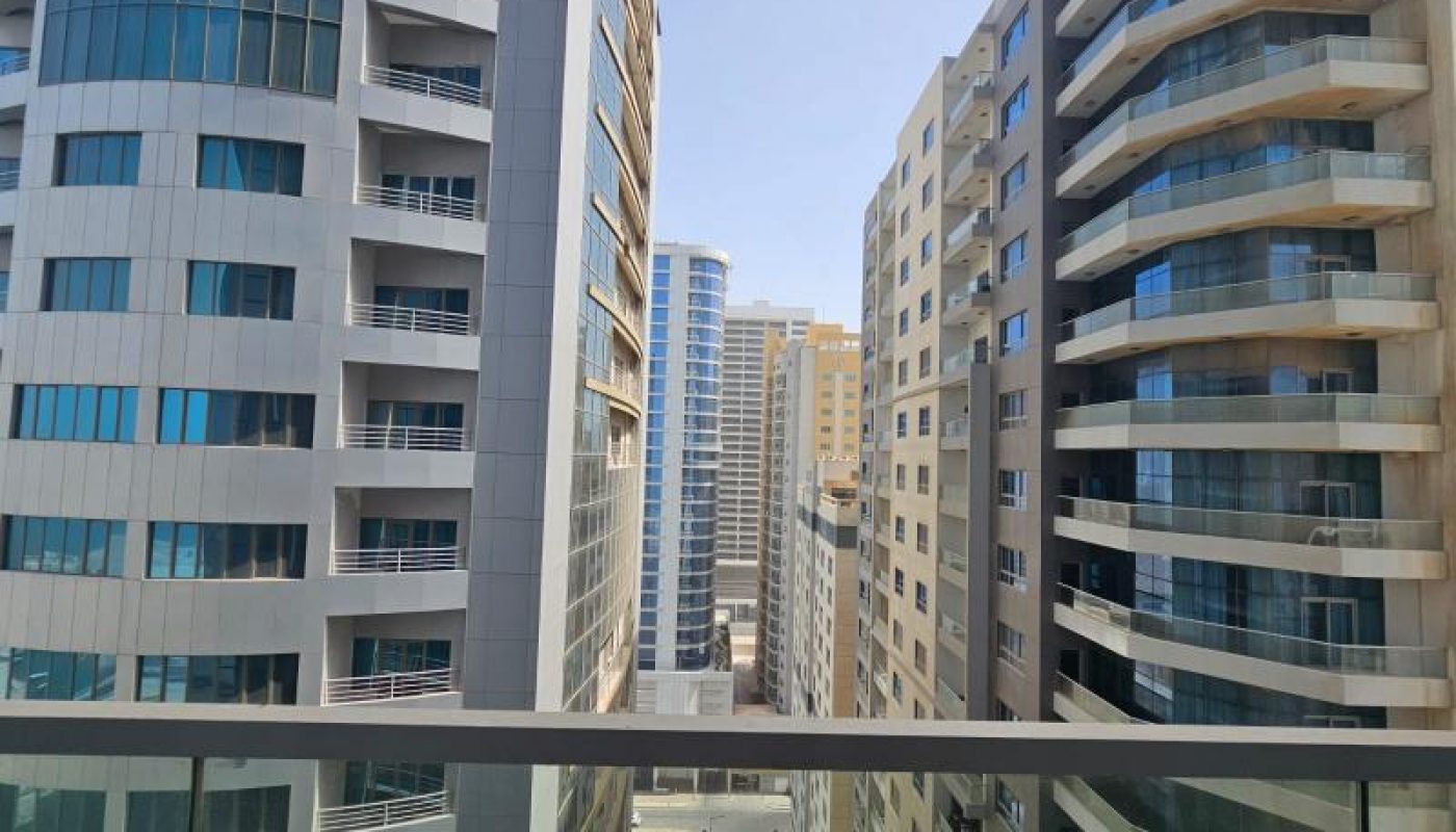Photo of several modern high-rise apartment buildings seen from a balcony, with clear blue sky and a narrow street below.