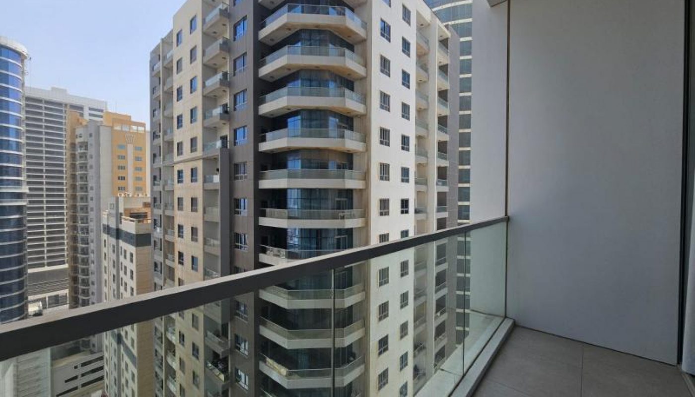 View from a balcony with glass railing overlooking modern high-rise apartment buildings in a city.