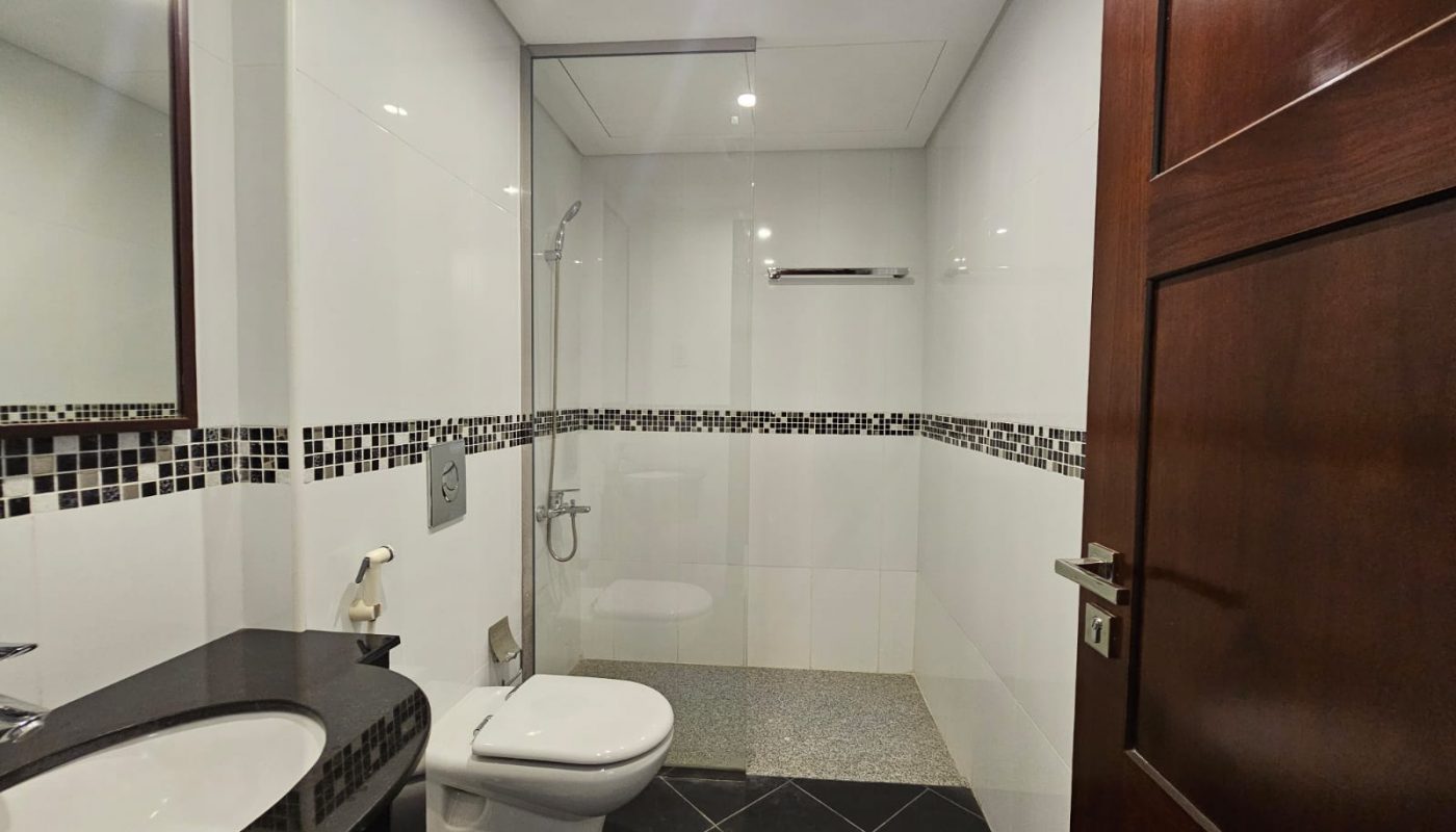 Modern bathroom with black-and-white tile design, wall-mounted toilet, sink with countertop, and a glass-enclosed shower area.