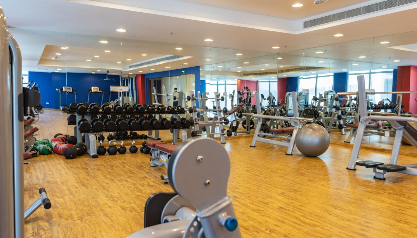 A spacious gym with wooden floors, weight racks, benches, exercise machines, a stability ball, and mirrored walls.