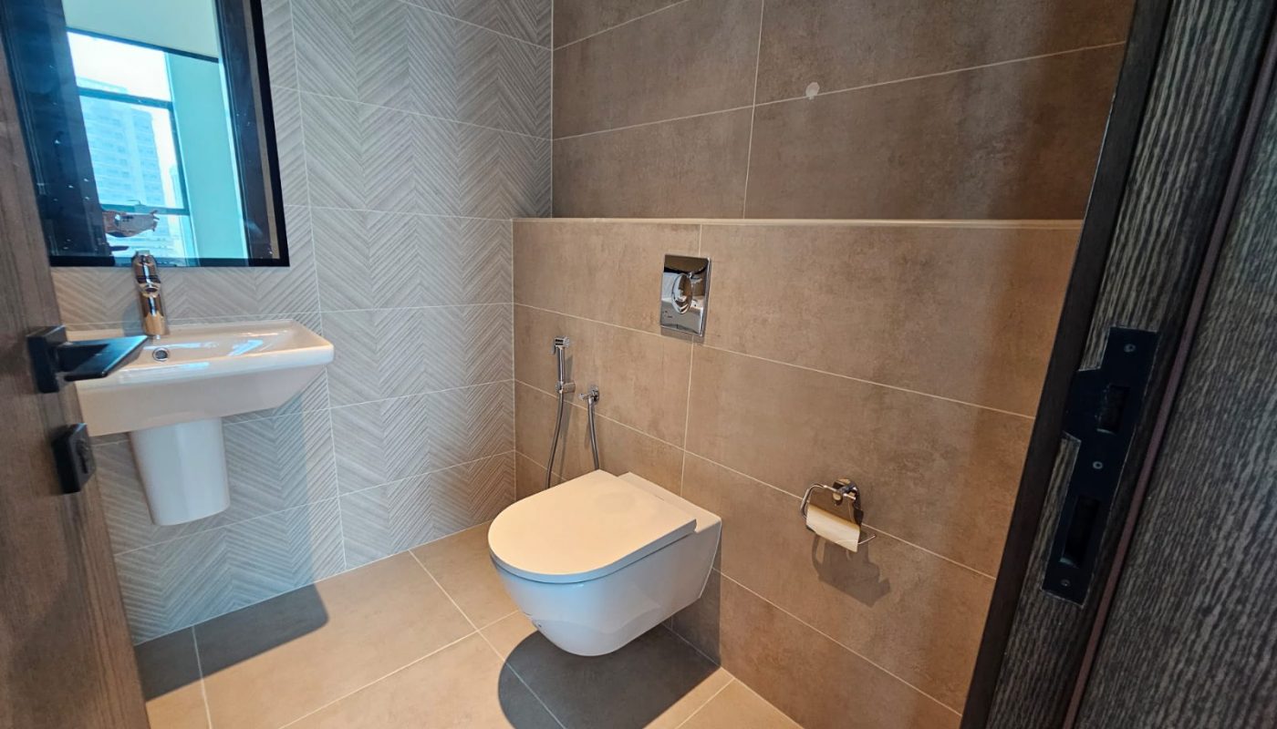 Modern bathroom with a wall-mounted toilet, a bidet spray, a toilet paper holder, a sink with a mirror, and beige tiled walls and floor.