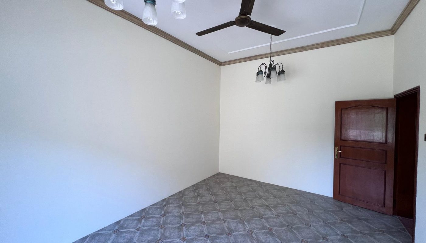 Empty room with light-colored walls, patterned tile floor, a ceiling fan, two light fixtures, and a wooden door slightly open.