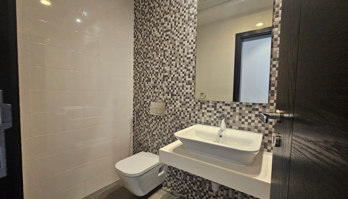 Modern bathroom with a wall-mounted toilet, a rectangular sink on a floating counter, a large mirror, and black-and-white mosaic tile wall.