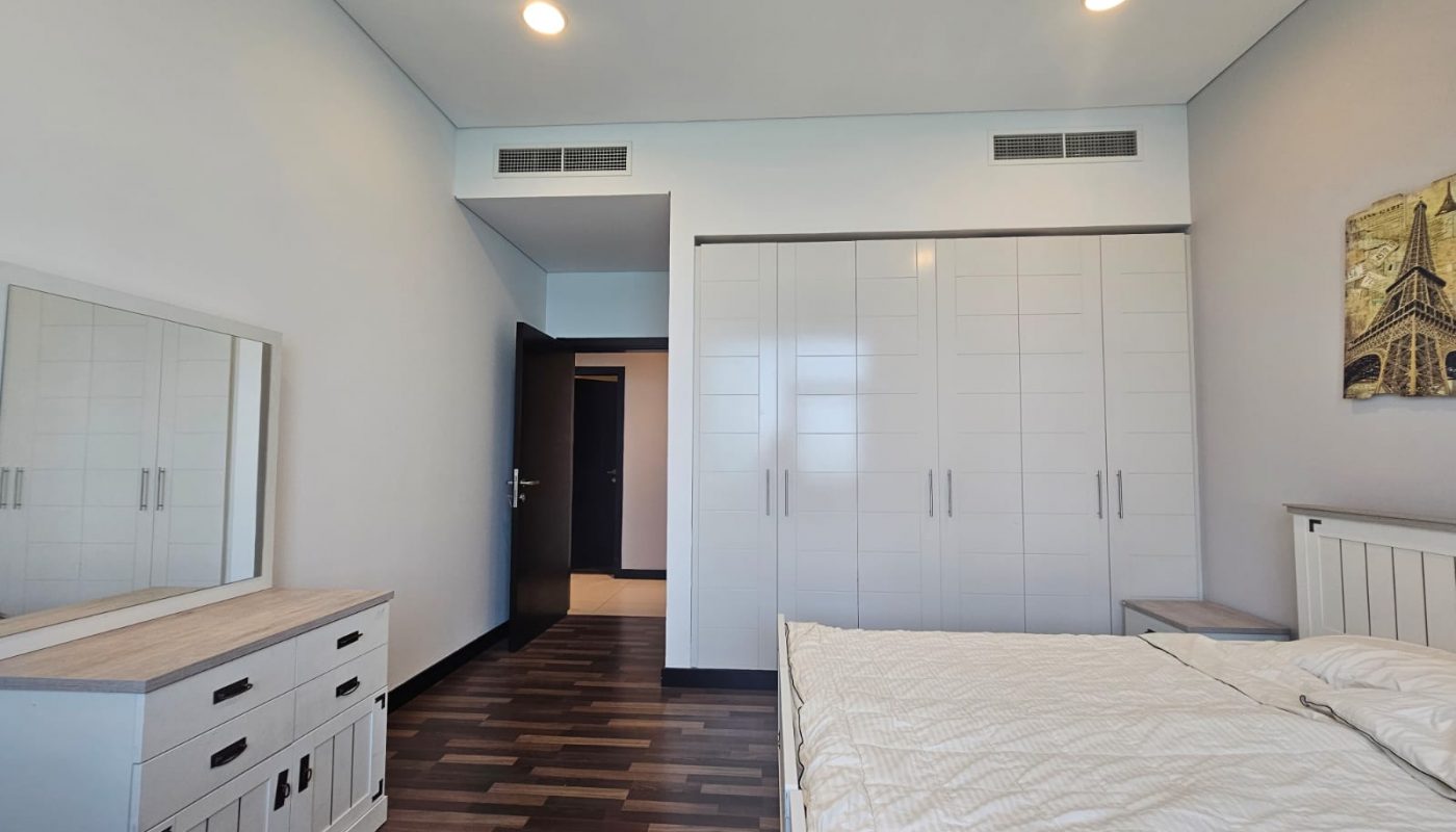 A bedroom with a bed, white wardrobe, dressing table with mirror, wooden floor, and a wall art of the Eiffel Tower.