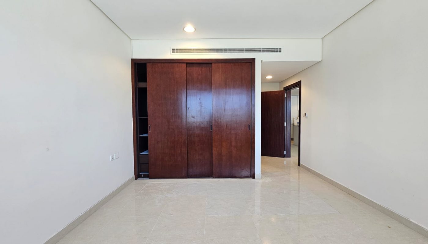 Empty room with beige tiled floor, white walls, a ceiling light, dark wooden sliding closet doors, and an open door leading to another area.