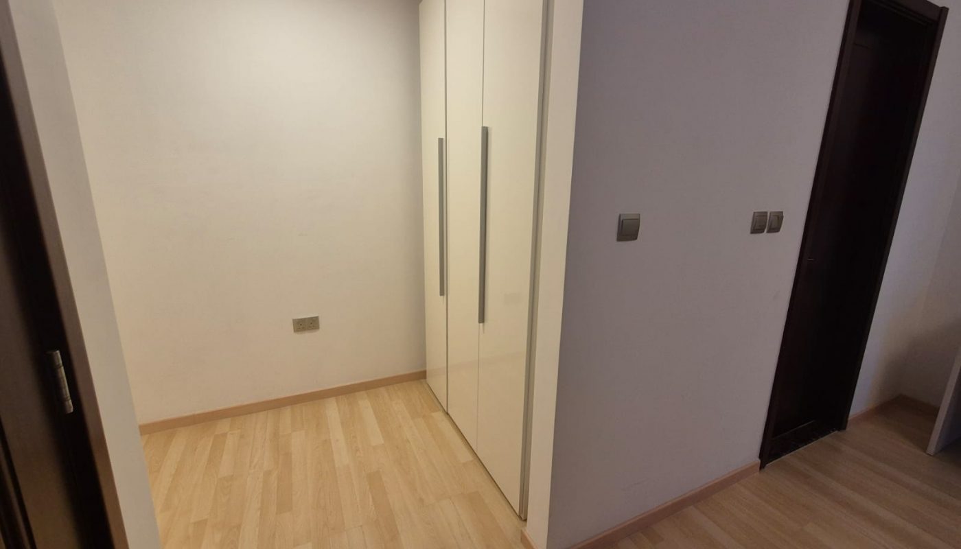 A small room with light wood flooring, white walls, a white wardrobe with vertical handles, and two dark door frames.