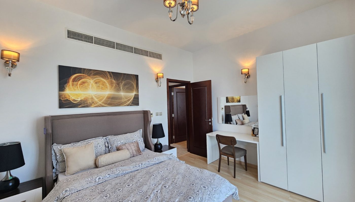 Modern bedroom with a double bed, patterned bedding, two black lamps, wall art above the headboard, a white wardrobe, a dressing table with a mirror, and ceiling lights.