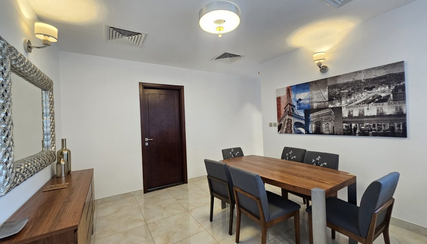 A modern dining room with a wooden table and six chairs, a sideboard with decor, tiled floor, wall art, and overhead lights.