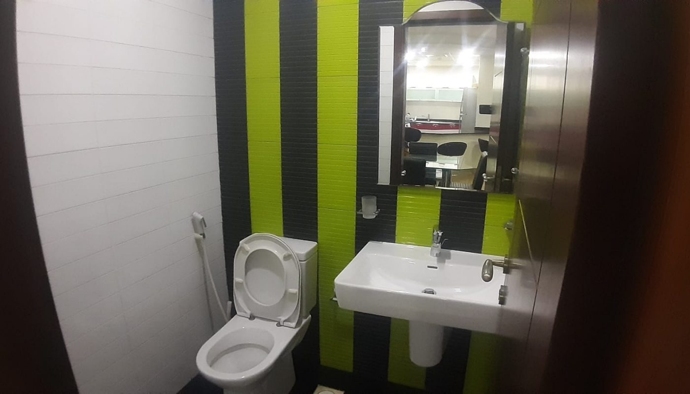 A bathroom with a toilet, a wall-mounted sink, a mirror, and black and green striped wall tiles.