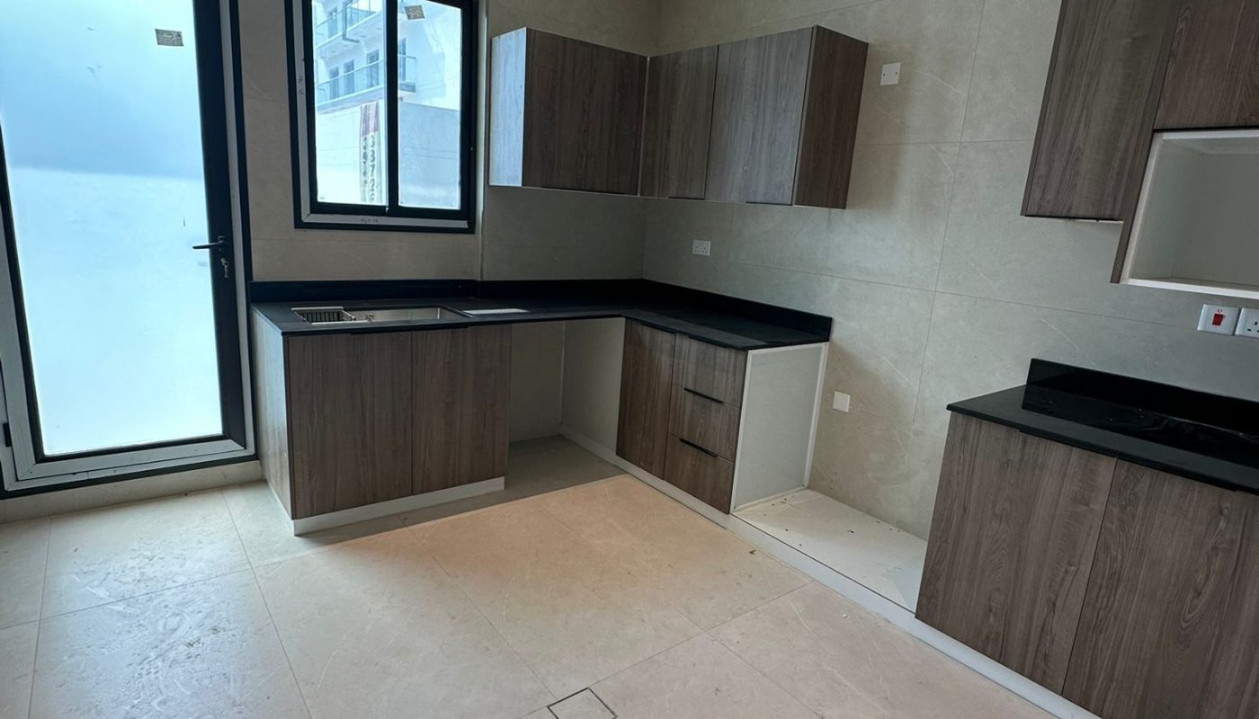 Modern kitchen with dark countertops, wooden cabinets, beige tile floor, and large frosted glass door and windows allowing natural light into the room.
