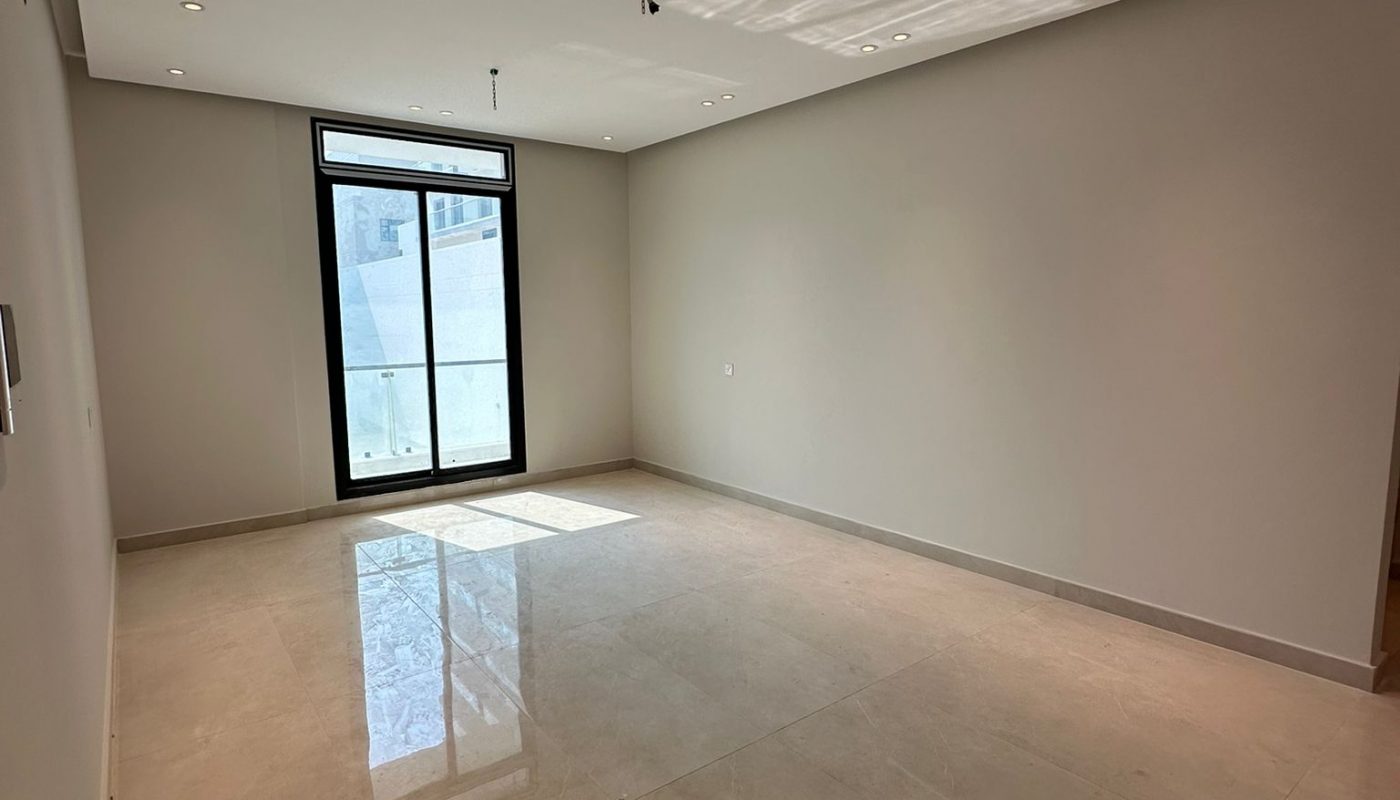 Empty room with beige tiled floor, light gray walls, recessed ceiling lights, a large window, and an exposed electrical fixture on the ceiling.
