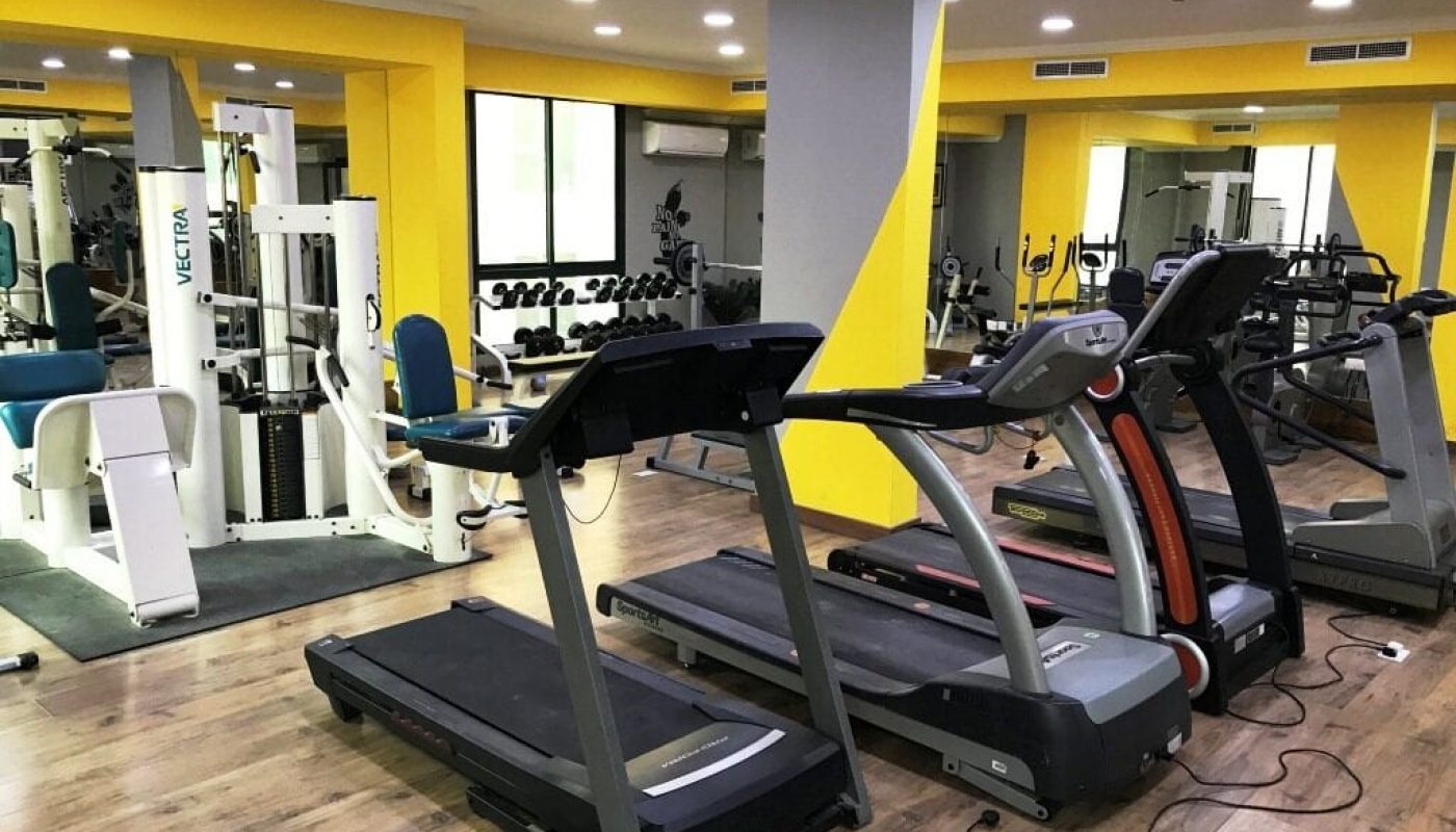 A gym with tread machines and yellow walls.
