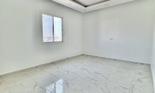 Luxury Apartment for Sale in Al Bahair: Step into this stunning empty room with marble floors and a ceiling fan.