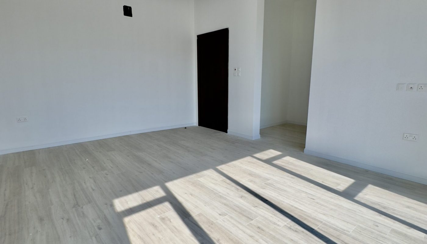A luxury 5BR villa in the Saar area, featuring an empty room with white walls and wood floors.