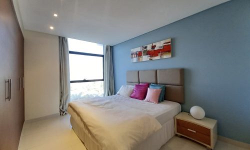 A luxury bedroom with blue walls and a white bed, featuring a balcony.