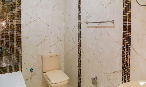 Furnished apartment with tiled bathroom walls and toilet.