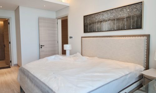 Fully Furnished Bedroom with a White Bed and a Painting on the Wall in Amazing Facilities Apartment for Rent in Juffair.