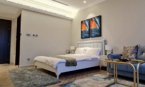 A beautiful studio for rent in Seef with a blue couch and a painting on the wall.