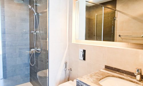 Luxury bathroom with glass shower stall and sink in a 1BR flat for sale in Seef.