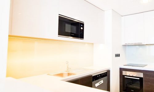 A luxury flat for sale in Seef with a white kitchen featuring a microwave and a sink.