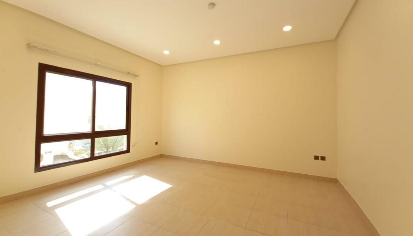Empty room with beige tiled floor, cream-colored walls, recessed ceiling lights, and a large window letting in natural light.