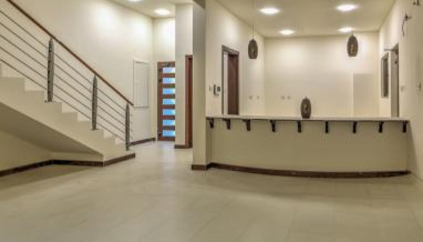 Spacious modern interior with tiled floor, staircase with metal railing on the left, and a reception counter with pendant lights on the right.