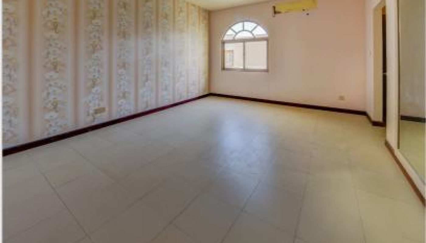 Empty room with tiled floor, floral wallpaper on one wall, a window with an arched top, a ceiling light fixture, wall-mounted AC unit, and a large mirror on the right.