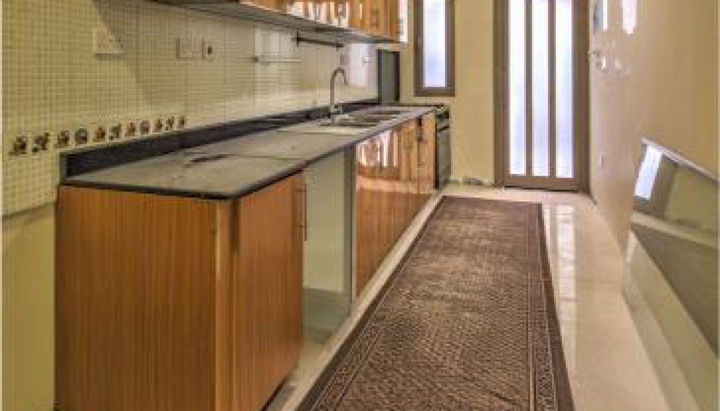 Modern galley kitchen with wooden cabinets, long countertop, under-cabinet sink, tiled backsplash, and a brown runner rug on a marble floor.