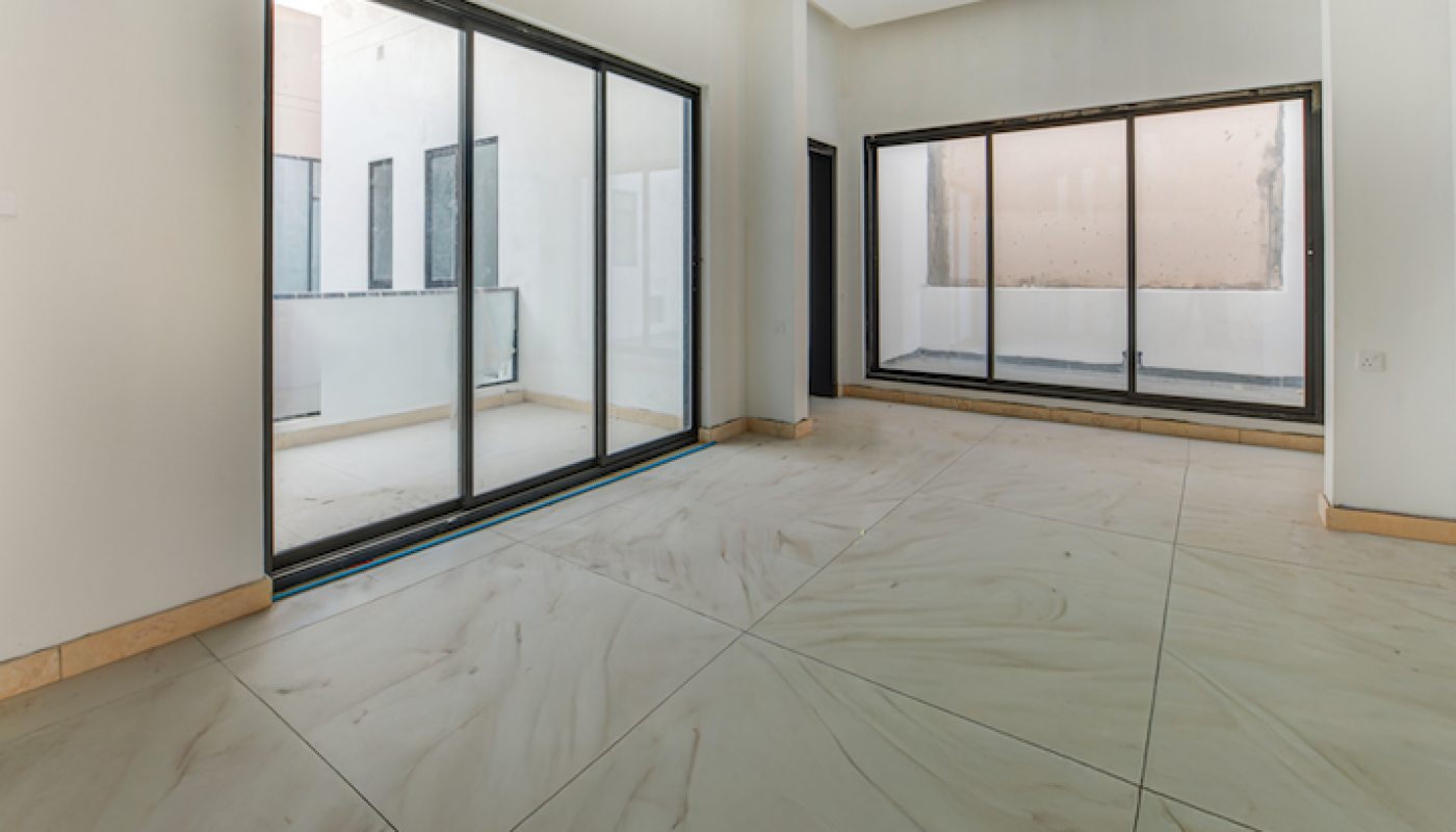 Empty modern room with large off-white tile flooring, white walls, and wide glass sliding doors leading to an outdoor area.