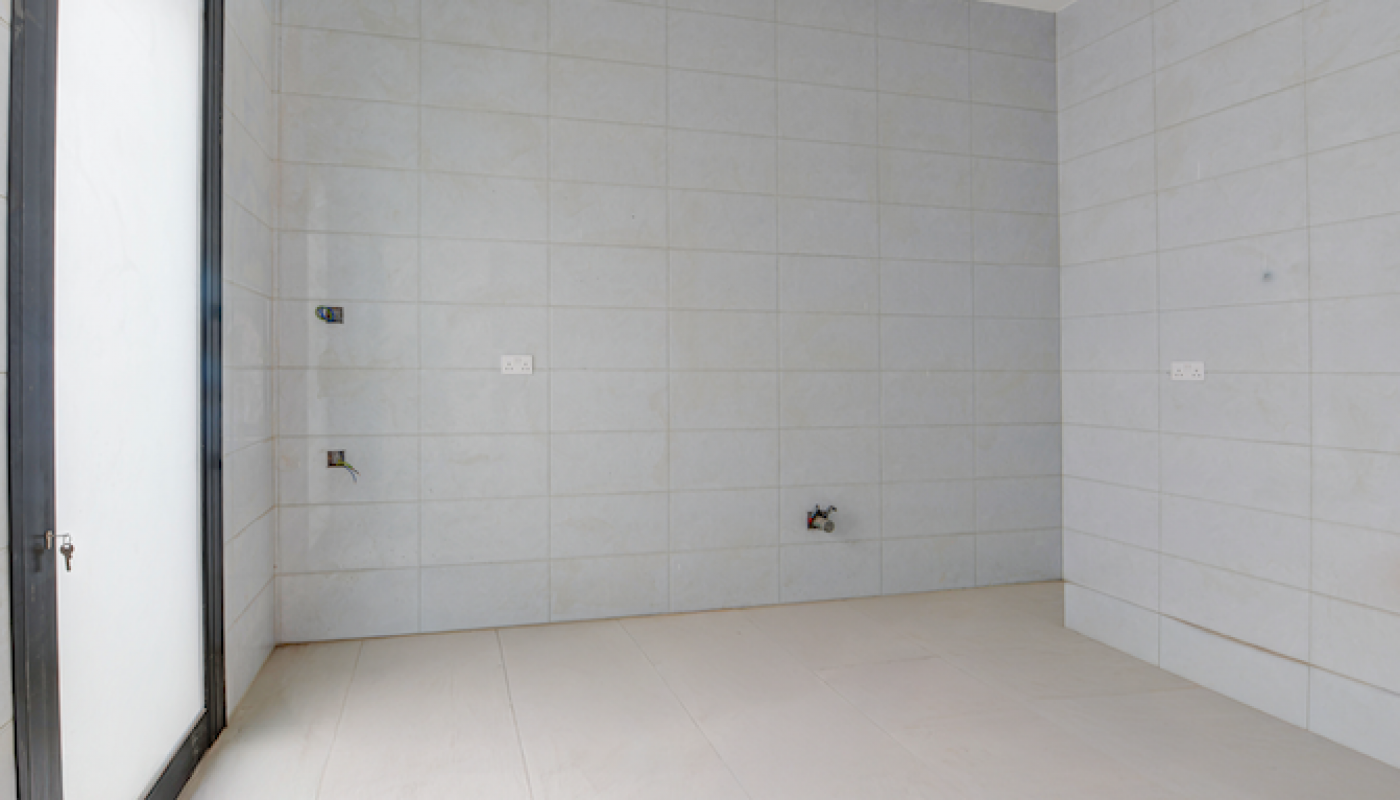 Empty, unfurnished room with tiled walls and floor, a large frosted glass door on the left, and visible utility connections on the walls.