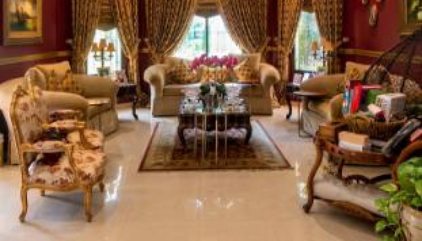 Elegant living room with ornate furniture, patterned drapes, artwork on burgundy walls, and polished tile floor, featuring a central coffee table and decorative plants.