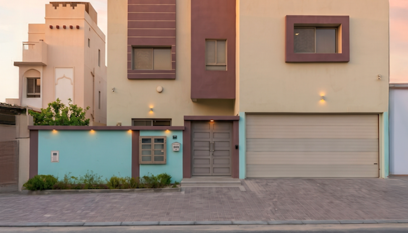 Modern two-story house with a flat roof, large garage, and pastel-colored facade, photographed at sunset from the street.