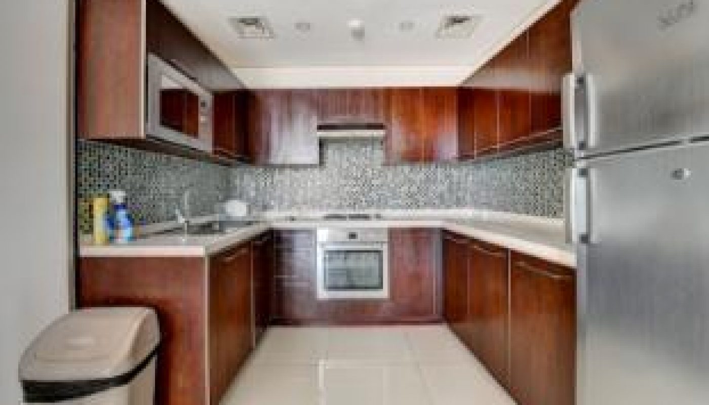 Modern kitchen with dark wood cabinets, stainless steel appliances, tiled backsplash, and a large trash bin on a white tiled floor.