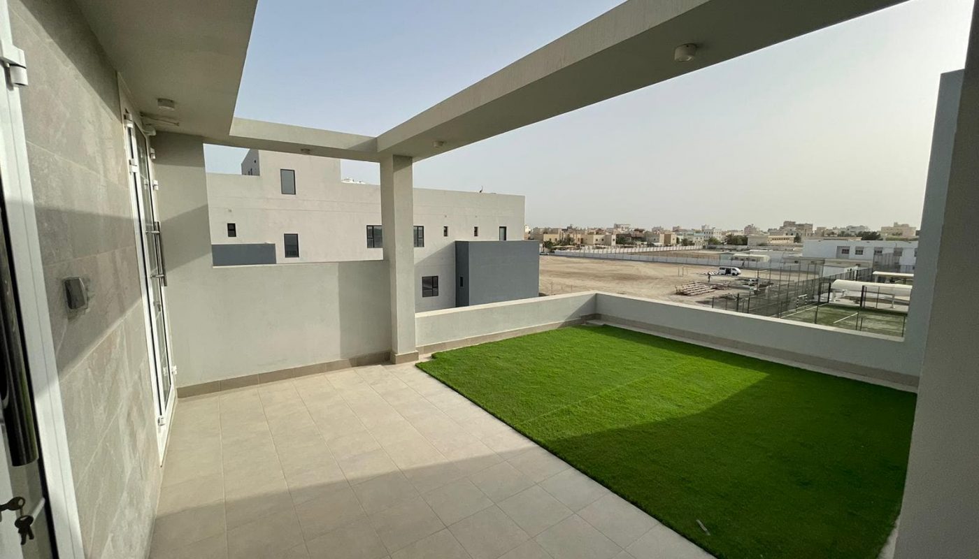 A luxury villa with a grass lawn and balcony overlooking an apartment building.