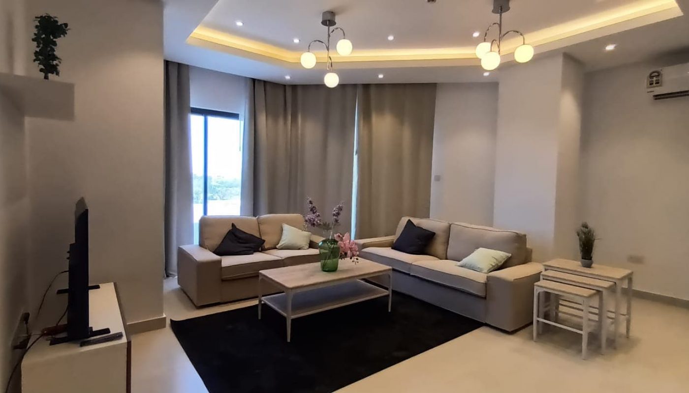 Brand New Living Room with White Couch and TV in 3BR Apartment for Rent in Al Janabiyah.