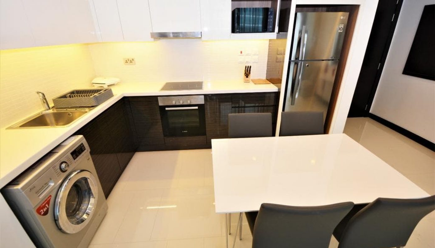 A small kitchen with a washing machine and refrigerator in an exquisite 1BR apartment for rent in Juffair with sea view.