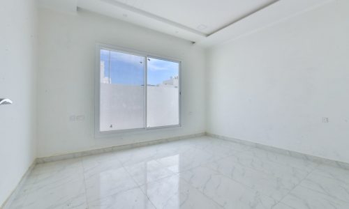 A white tiled room with a window and a door in an amazing villa.